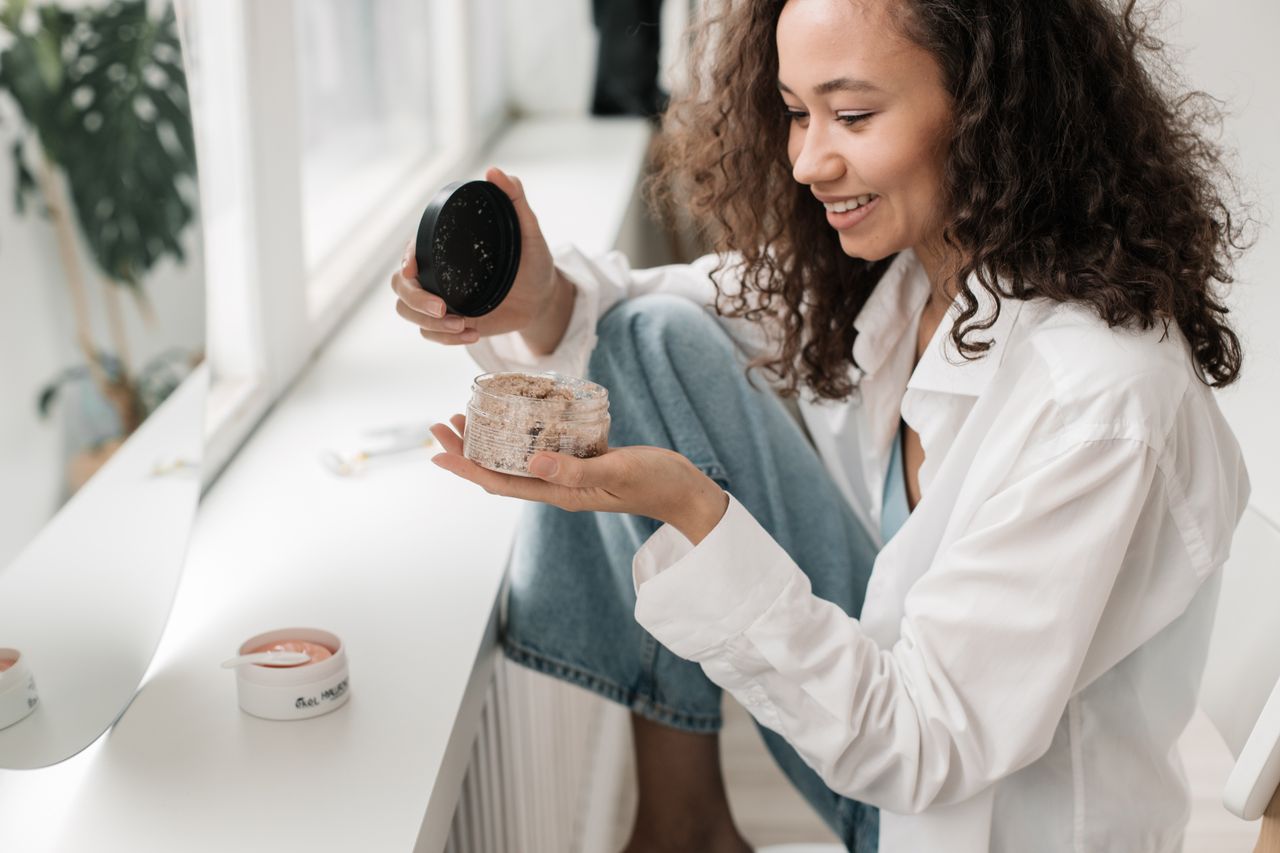 Smiling woman applying skincare products, embracing self-care in a bright indoor setting.